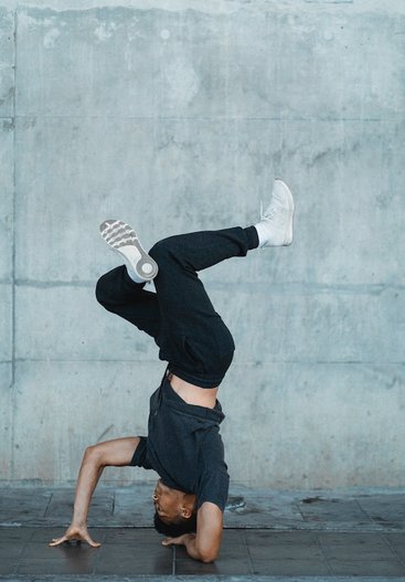 Man is aan het breakdancen. Hij steunt, ondersteboven, op een hand en een onderarm, voeten in de lucht. Hij heeft zijn eigen beweging en ritme gevonden.